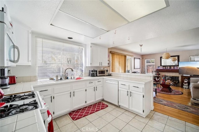 kitchen featuring a peninsula, tile counters, a sink, and white appliances