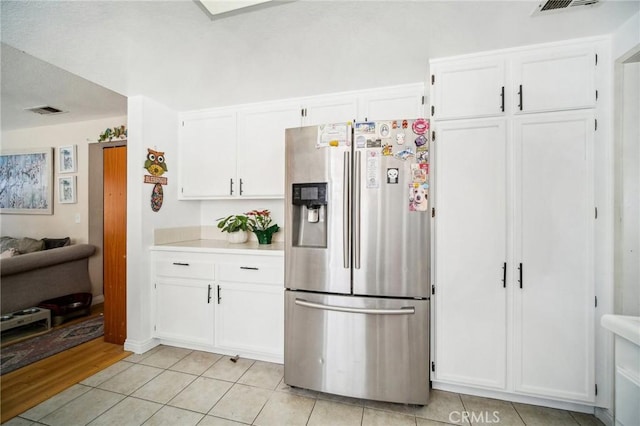 kitchen with white cabinets, stainless steel fridge, light tile patterned flooring, visible vents, and light countertops