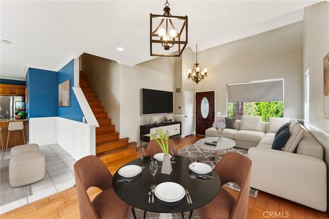 living area with stairway, a towering ceiling, wood finished floors, a notable chandelier, and wainscoting