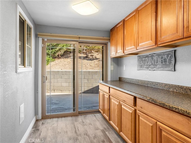 doorway with light wood-style flooring, baseboards, and a textured wall
