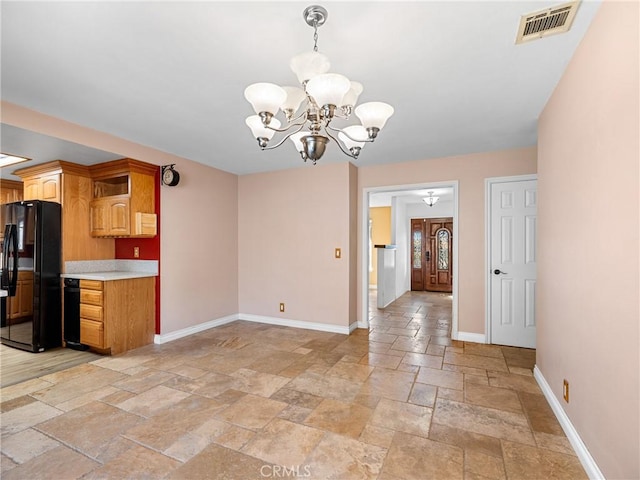 kitchen with stone tile floors, baseboards, freestanding refrigerator, a chandelier, and light countertops