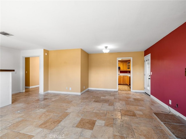 spare room featuring stone tile floors, baseboards, and visible vents