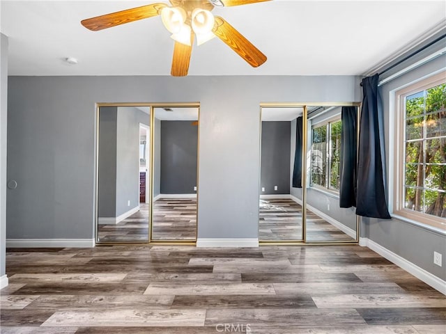 unfurnished bedroom featuring two closets, ceiling fan, baseboards, and wood finished floors