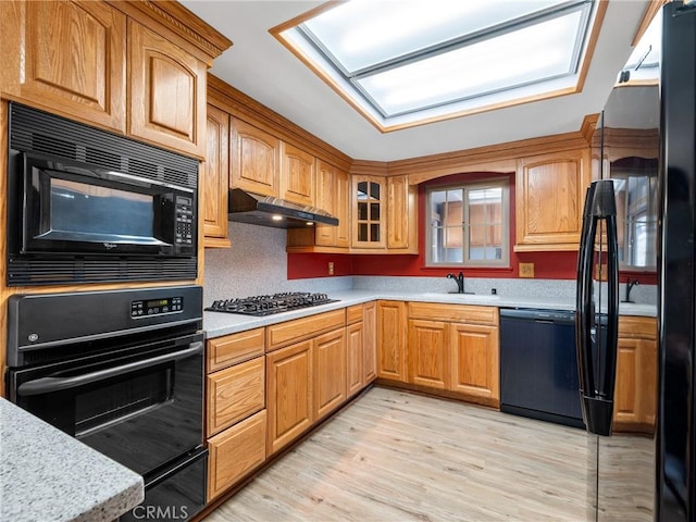 kitchen with under cabinet range hood, a sink, light wood-type flooring, black appliances, and glass insert cabinets