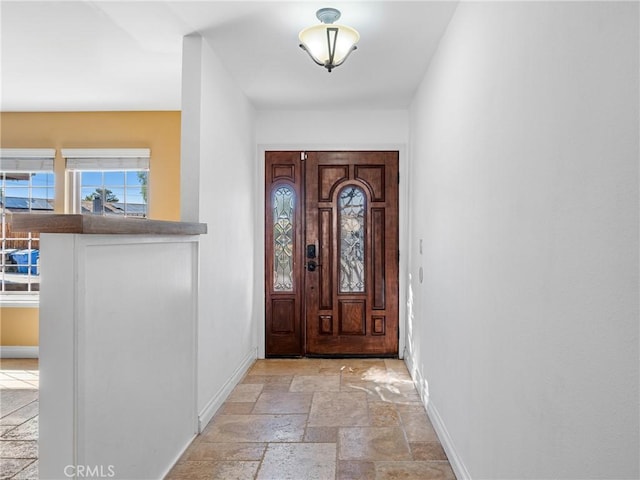 foyer entrance with baseboards and stone tile flooring