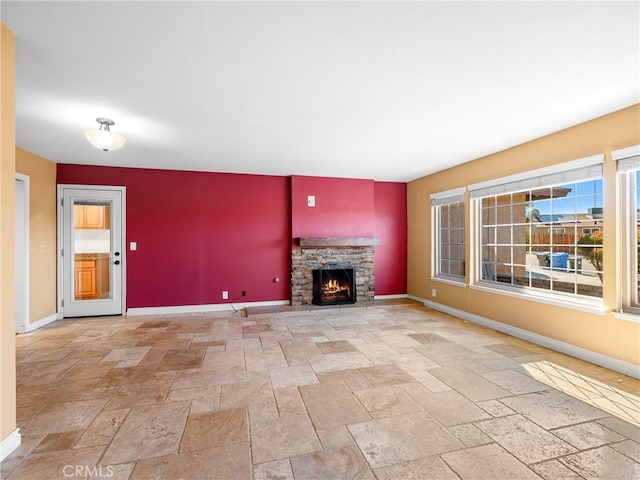 unfurnished living room featuring a stone fireplace, stone tile floors, baseboards, and plenty of natural light