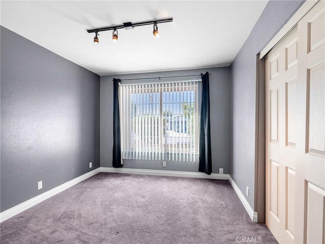 empty room featuring carpet, rail lighting, and baseboards