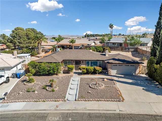 ranch-style home featuring concrete driveway, an attached garage, fence, a mountain view, and a residential view