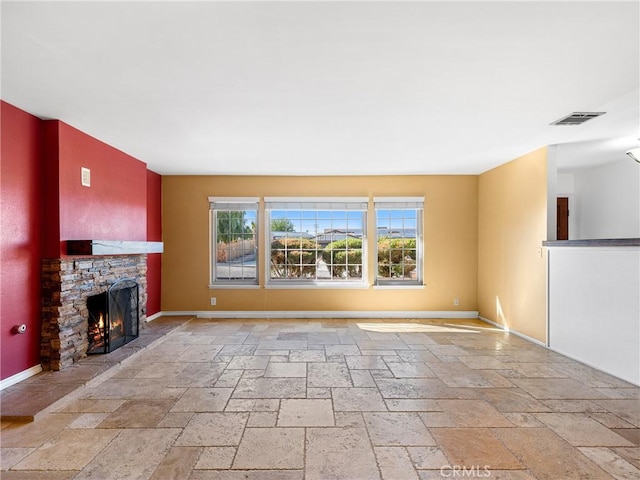 unfurnished living room featuring baseboards, stone tile floors, a stone fireplace, and visible vents