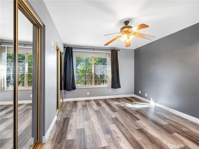 unfurnished room featuring a ceiling fan, baseboards, a healthy amount of sunlight, and wood finished floors