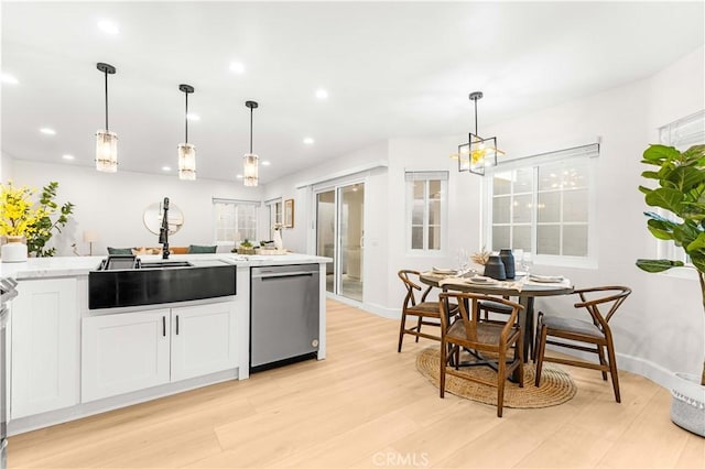 kitchen with a sink, light countertops, light wood-type flooring, dishwasher, and decorative light fixtures