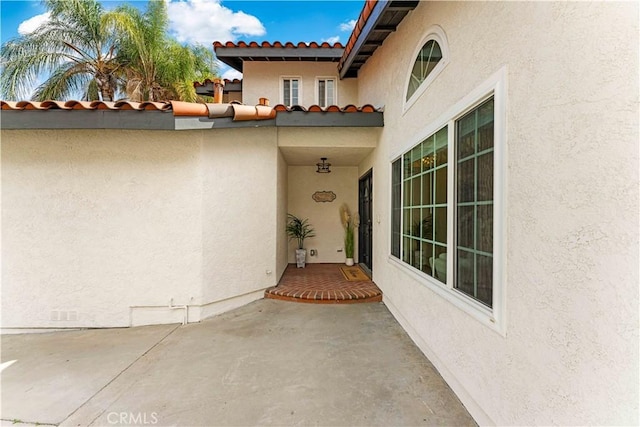 view of exterior entry with stucco siding and a tiled roof