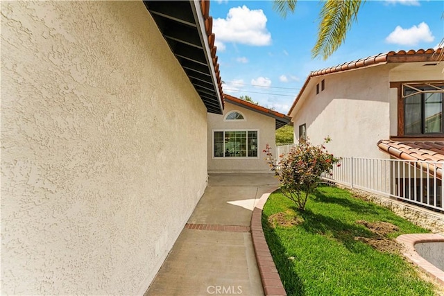 view of side of property featuring stucco siding, fence, and a tile roof