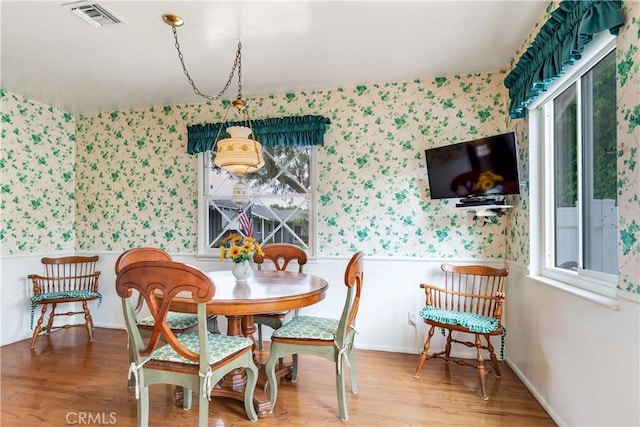 dining space featuring baseboards, visible vents, wood finished floors, and wallpapered walls