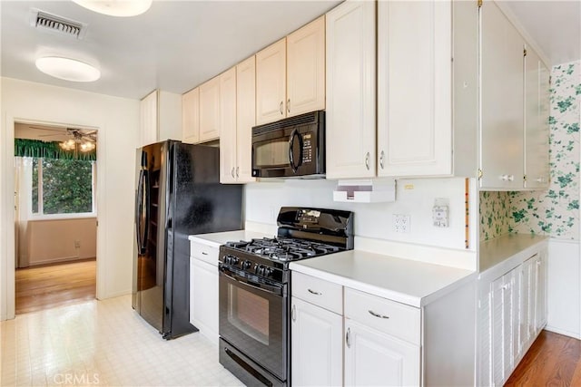 kitchen featuring white cabinets, light countertops, visible vents, light wood-type flooring, and black appliances