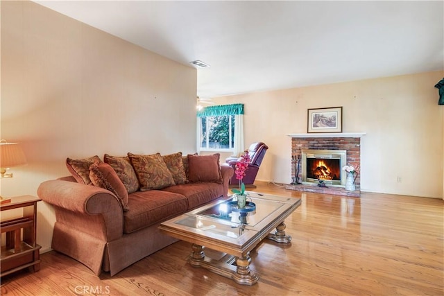 living room featuring a brick fireplace, wood finished floors, and visible vents