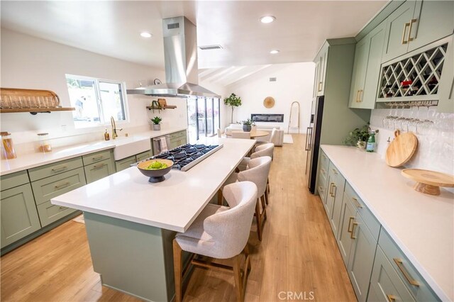 kitchen with island exhaust hood, a kitchen breakfast bar, green cabinetry, and stainless steel gas cooktop