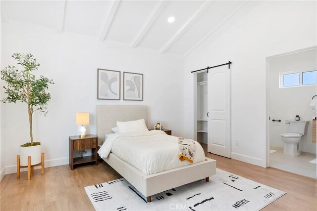 bedroom with a barn door, connected bathroom, vaulted ceiling with beams, light wood finished floors, and baseboards