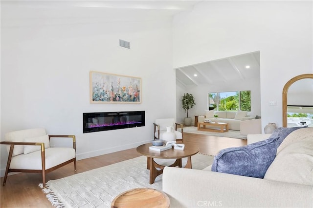 living area with wood finished floors, a glass covered fireplace, baseboards, beam ceiling, and visible vents