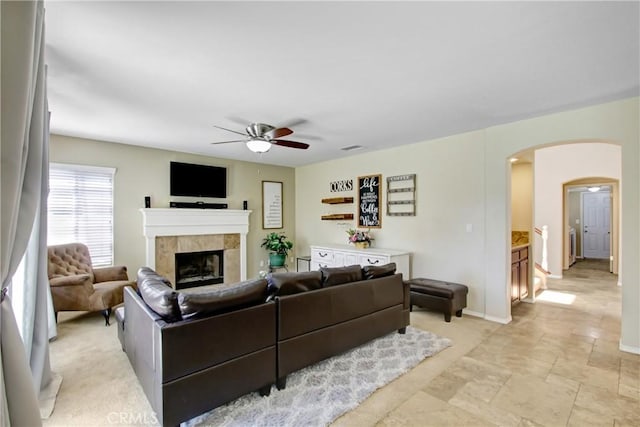 living room featuring baseboards, ceiling fan, a tile fireplace, arched walkways, and stone finish flooring