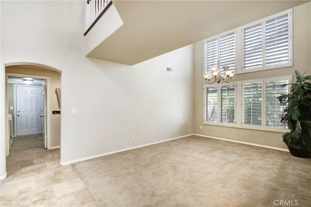 empty room with visible vents, baseboards, a high ceiling, a chandelier, and arched walkways