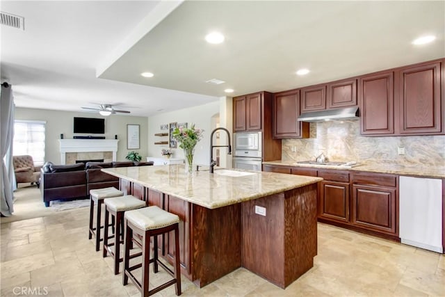 kitchen featuring a ceiling fan, visible vents, a tile fireplace, a sink, and light stone counters