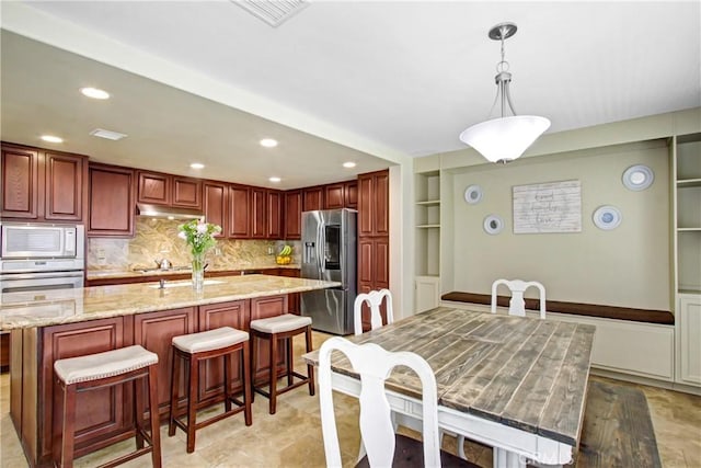kitchen with light stone countertops, stainless steel appliances, tasteful backsplash, under cabinet range hood, and visible vents