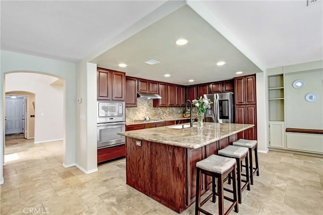 kitchen with a kitchen breakfast bar, a sink, baseboards, under cabinet range hood, and stainless steel appliances