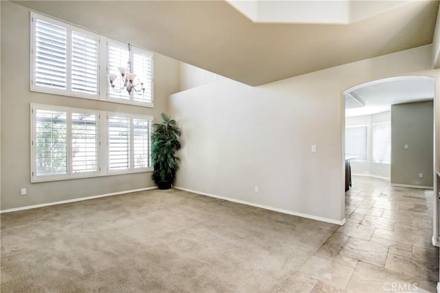 empty room with a notable chandelier, arched walkways, baseboards, a towering ceiling, and stone tile flooring