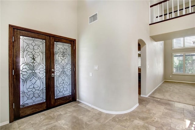entryway featuring arched walkways, visible vents, baseboards, and a towering ceiling