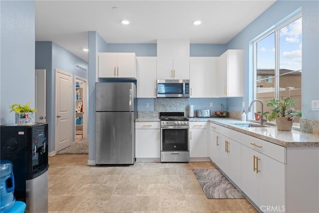 kitchen featuring light stone countertops, appliances with stainless steel finishes, a sink, white cabinetry, and decorative backsplash