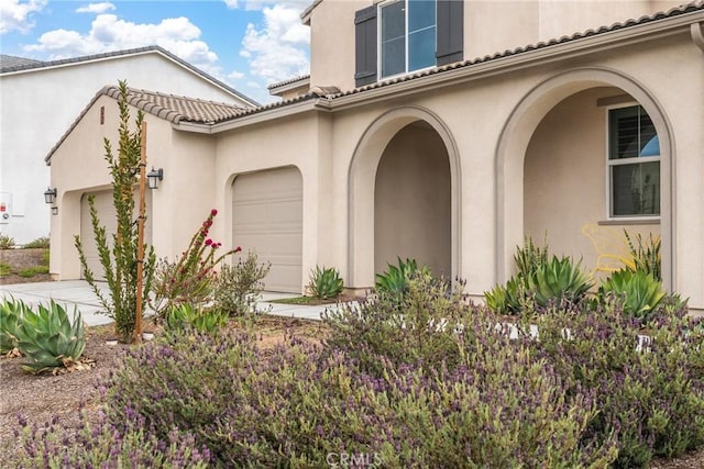 property entrance featuring concrete driveway, stucco siding, an attached garage, and a tiled roof