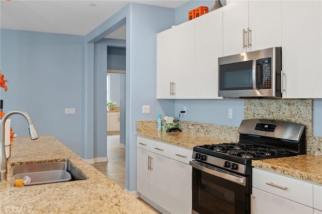 kitchen featuring light stone countertops, a sink, stainless steel appliances, white cabinetry, and backsplash