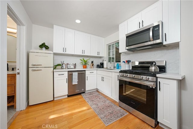 kitchen with light countertops, light wood-type flooring, appliances with stainless steel finishes, and white cabinetry