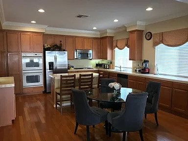 38728 Falkirk Dr, Murrieta, CA 92563 - kitchen featuring stainless steel appliances, ornamental molding, brown cabinets, light countertops, and dark wood-style floors