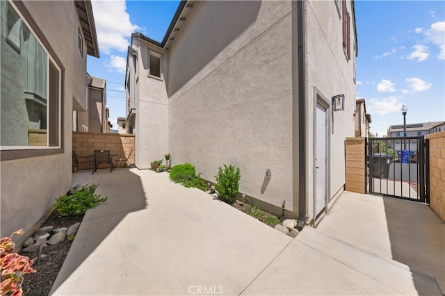 view of side of home featuring a gate, a patio, stucco siding, and fence