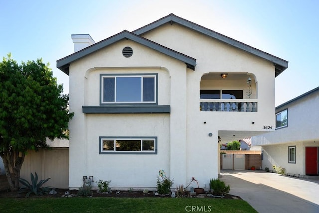 view of front of property with stucco siding, fence, driveway, a balcony, and a carport