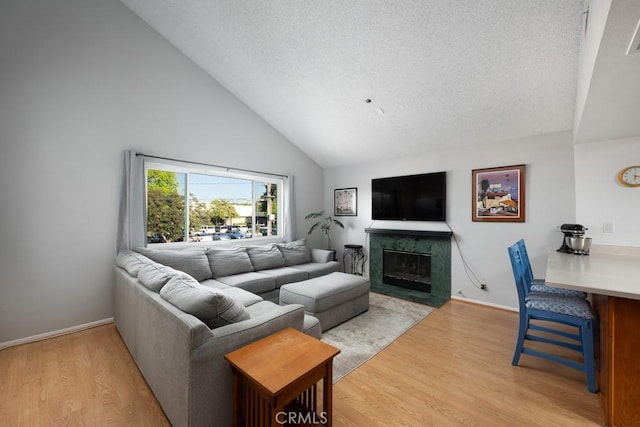 living room with high vaulted ceiling, light wood-style floors, a fireplace, a textured ceiling, and baseboards