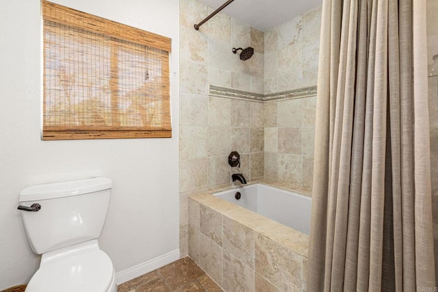 bathroom featuring stone tile flooring, baseboards, tiled shower / bath combo, and toilet