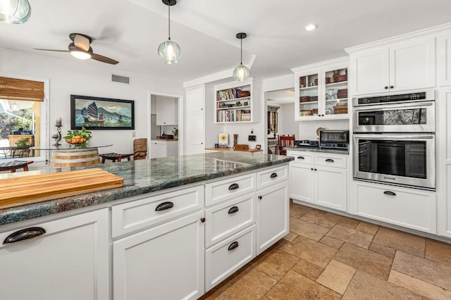 kitchen featuring a ceiling fan, hanging light fixtures, stone tile floors, double oven, and white cabinets