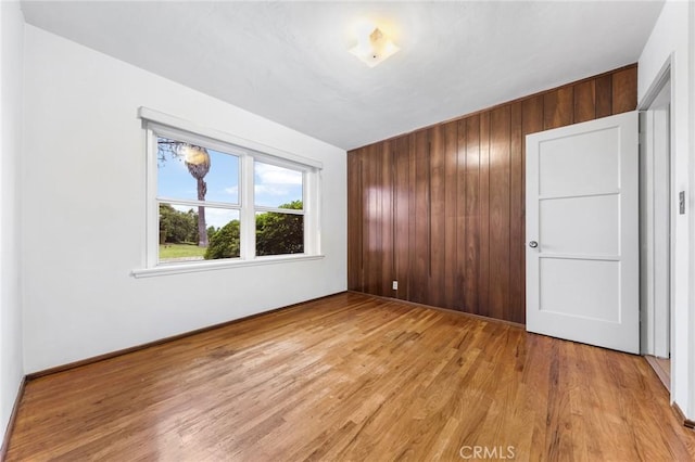 empty room with light wood-type flooring, baseboards, and wood walls