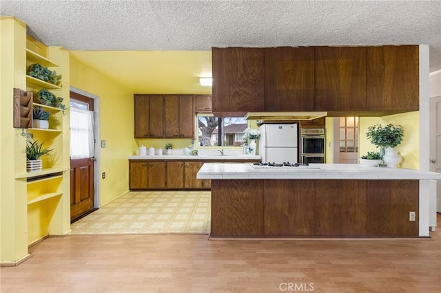 kitchen with open shelves, white appliances, light wood-style floors, and tile countertops