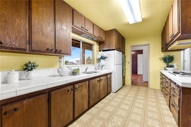 kitchen featuring light floors, white appliances, a sink, and tile countertops