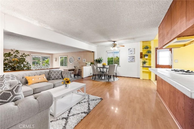 living area with a textured ceiling, light wood finished floors, and a ceiling fan