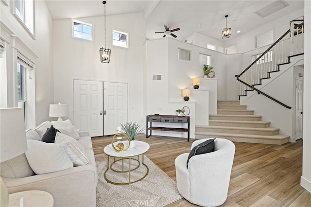 living area with high vaulted ceiling, stairs, a ceiling fan, visible vents, and wood finished floors