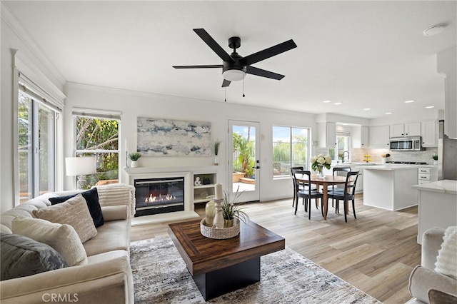26 Apache Dr, Trabuco Canyon, CA 92679 - living area featuring healthy amount of natural light, a ceiling fan, crown molding, a glass covered fireplace, and light wood-type flooring