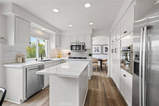 kitchen with arched walkways, appliances with stainless steel finishes, white cabinets, a sink, and a center island