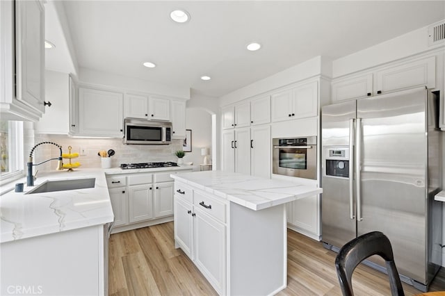 kitchen with light stone countertops, appliances with stainless steel finishes, a kitchen island, a sink, and white cabinetry