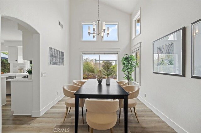 dining space with arched walkways, an inviting chandelier, light wood-style flooring, and baseboards