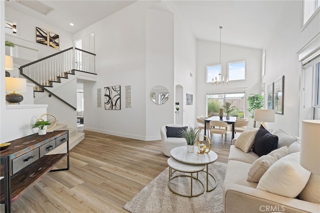 living area with a chandelier, high vaulted ceiling, wood finished floors, and stairs